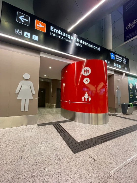 Entrada a los baños de un aeropuerto internacional con señalización clara para sanitarios de mujeres, baños familiares y accesibles para personas con discapacidad, junto al cartel de embarque internacional e iluminación moderna.