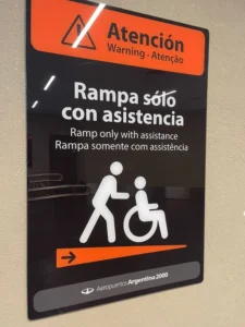 Cartel informativo en un aeropuerto de Argentina que advierte que la rampa solo puede utilizarse con asistencia, mostrando un ícono de una persona empujando una silla de ruedas.