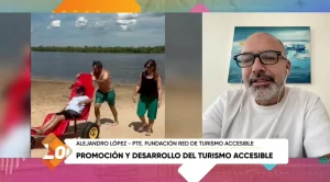 Captura de pantalla de un programa de TV sobre turismo accesible: a la izquierda, una persona en una silla anfibia roja en la playa mientras la empujan; a la derecha, un hombre con anteojos en videollamada. Zócalo: ‘Alejandro López – Pte. Fundación Red de Turismo Accesible’ y ‘Promoción y desarrollo del turismo accesible’ (Canal Local).